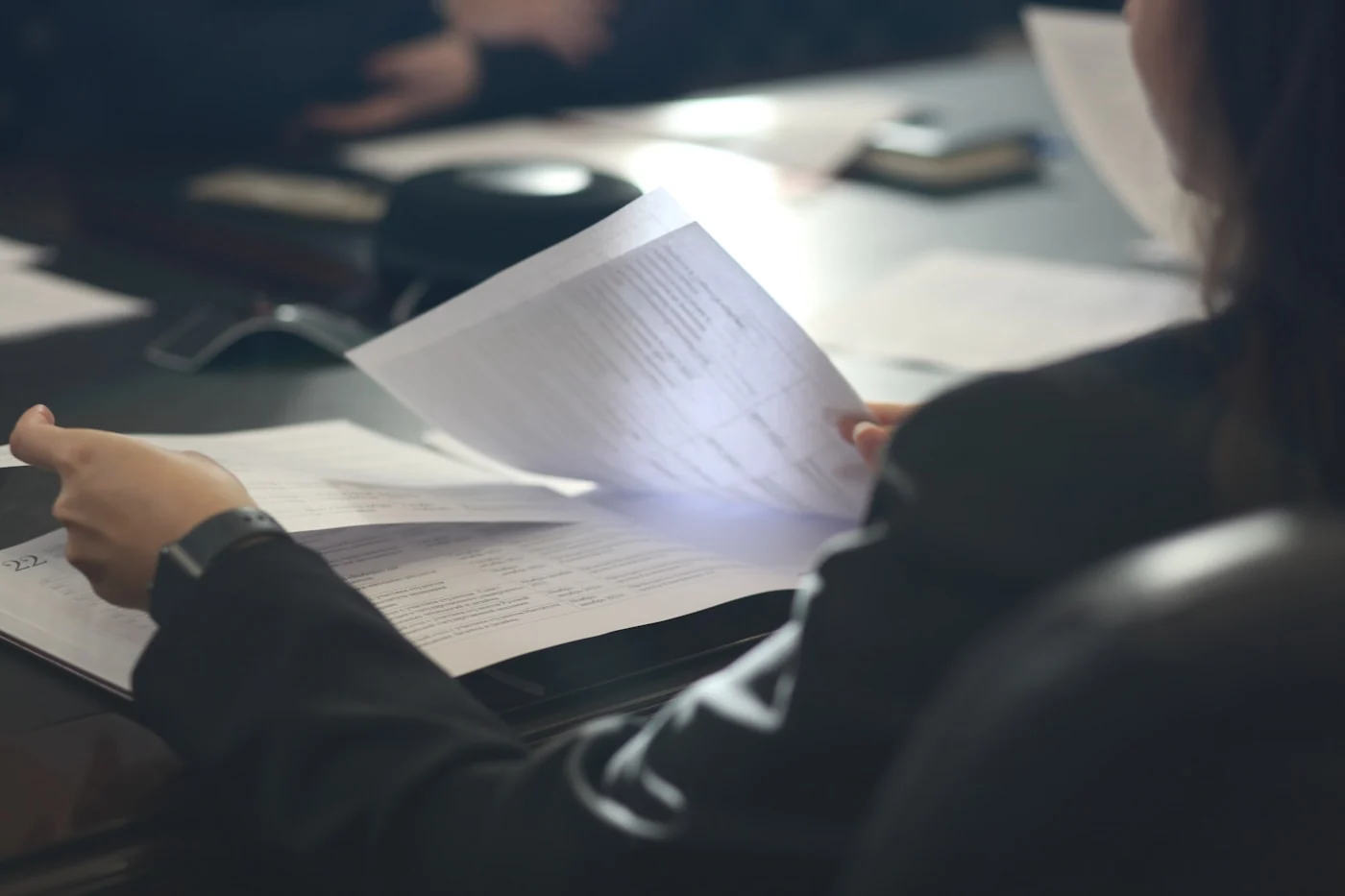 A person seated at a meeting table, leafing through the pages of a printed document.